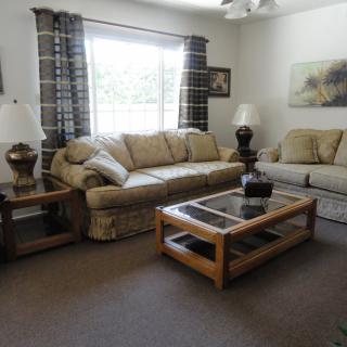 A cozy living room with comfortable sofas, a glass-top coffee table, and decorative lamps by the window.