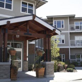 A modern apartment building with a wooden entrance canopy and potted plants.