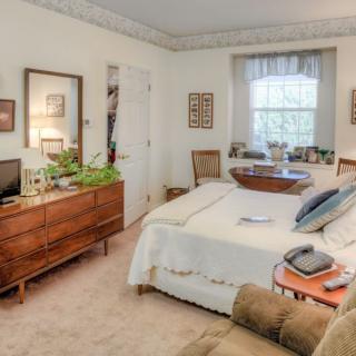 A cozy bedroom featuring a bed, dresser, and window with curtains.