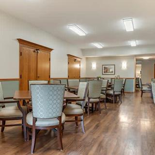 A spacious dining area with multiple tables and chairs, featuring wood flooring and soft lighting.