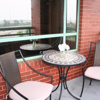 A small balcony with a decorative round table and two chairs adjacent to a brick wall.