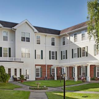 A three-story residential building with a well-maintained garden and lawn in the foreground.