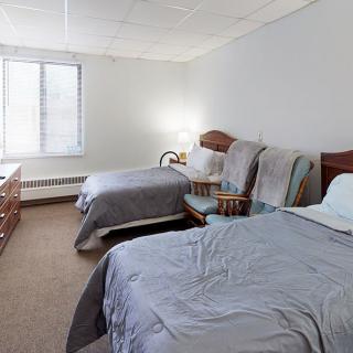 A cozy bedroom with two beds, a chair, and a window letting in natural light.