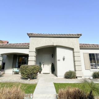 A charming residential house with a welcoming entrance and well-maintained landscaping under a clear blue sky.