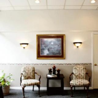 A well-decorated waiting room with two chairs, a table, wall sconces, and a painting on the wall.