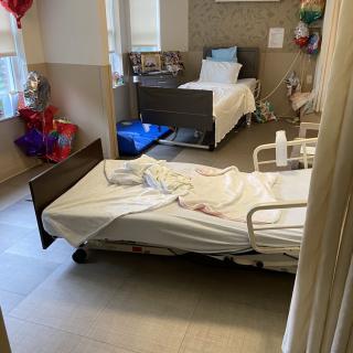 A hospital room with two beds and colorful balloons by the window.