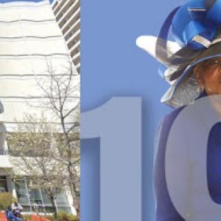 A stylish individual in a striking hat, set against a modern building backdrop.