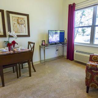 A cozy living room with a dining table, chairs, television, and a window with curtains.