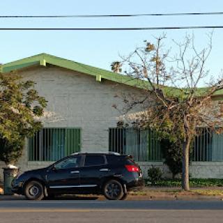 A black car parked in front of a residential building with green accents and a tree nearby.
