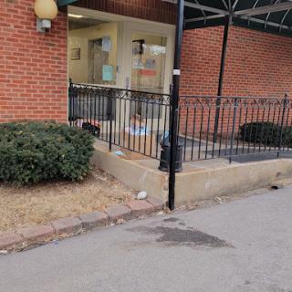 A view of a brick building's entrance with a fenced area and some landscaping.
