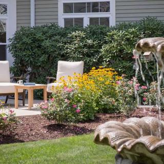 A serene garden with comfortable chairs, blooming flowers, and a decorative fountain.