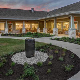 A beautifully landscaped courtyard with a central stone feature, surrounded by a modern building at dusk.