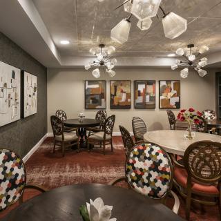 A stylish dining room featuring elegant lighting, art-adorned walls, and patterned furnishings.