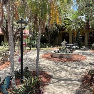 A serene garden pathway with a fountain surrounded by palm trees and well-maintained landscaping.