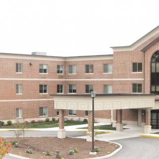 A three-story brick healthcare facility with a covered entrance and surrounding landscaping.