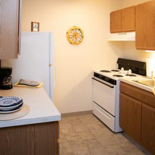A cozy kitchen featuring wooden cabinets, a stove, refrigerator, and a countertop with plates.