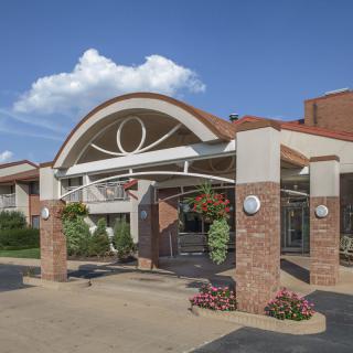 A modern building entrance with an arched design and brick pillars, surrounded by landscaped plants.
