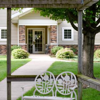 A tranquil garden with a white bench facing a building entrance.