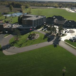 An aerial view of a complex surrounded by green fields and parking areas.