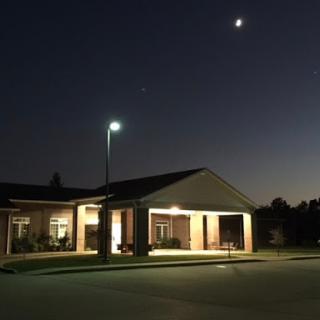 A serene night view of a building illuminated by streetlights, with the moon overhead.