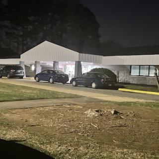 A quiet night scene featuring a building with cars parked outside, illuminated by outdoor lights.