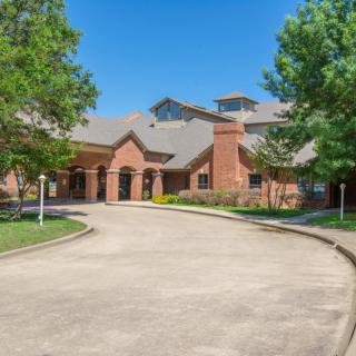 A picturesque brick house with a curved driveway and lush trees surrounding it.
