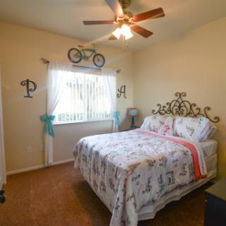 A cozy and inviting bedroom featuring a ceiling fan, bicycle decor, and floral-patterned bedding.