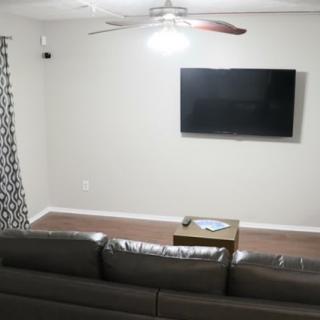 A minimalist living room with a sofa facing a wall-mounted television, a small table, and a ceiling fan overhead.