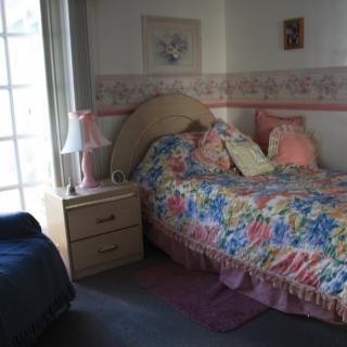 A cozy bedroom with floral bedding, a nightstand, and a lamp beside a large window.