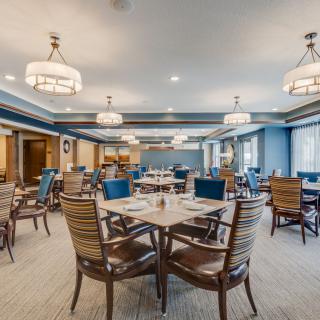 A spacious and elegantly decorated dining room with tables and chairs, illuminated by chandeliers.