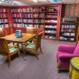 A cozy library reading room with bookshelves, a table, and comfortable chairs.