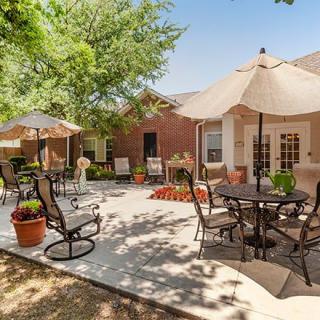 A sunny outdoor patio with tables, chairs, umbrellas, and potted plants.