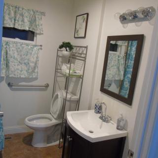 A neatly organized bathroom featuring a toilet, sink, mirror, and shelving unit with decor.