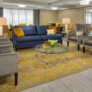 A modern living room with a blue sofa, gray chairs, a glass coffee table, and a patterned carpet.