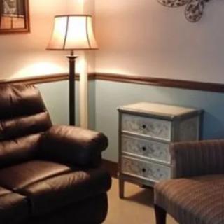 A cozy living room corner featuring a leather recliner, a floor lamp, and a small wooden cabinet.