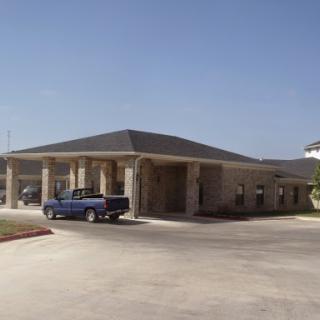 A view of a single-story building with a blue truck parked in the foreground.
