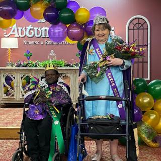 A joyful celebration featuring two crowned queens at a community event, surrounded by festive balloons and decorations.