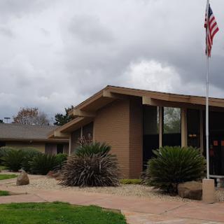 A building with a modern architectural design, surrounded by plants and an American flag under a cloudy sky.