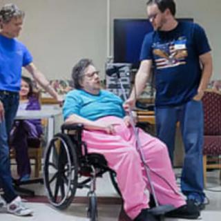 An elderly woman in a wheelchair is surrounded by family members during a visit in a hospital room.