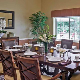 A well-decorated dining room with a large table set for a meal, surrounded by chairs and lush greenery by the window.