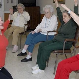A group of elderly individuals participating in a seated exercise or yoga session.