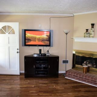 A cozy living room with a mounted television, brick fireplace, and hardwood flooring.