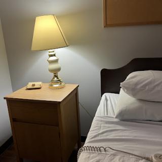 A cozy bedroom setup featuring a nightstand with a lamp beside an unmade bed.