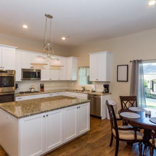 A modern kitchen with white cabinets, granite countertops, and a dining area.