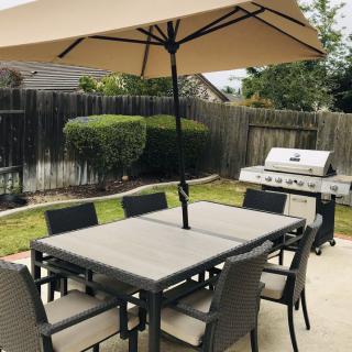 A backyard patio with a dining set and an umbrella next to a grill.