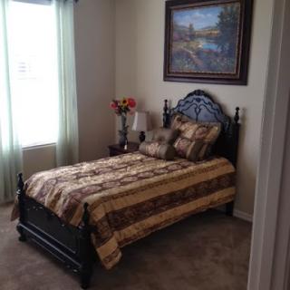 A cozy and well-decorated bedroom featuring a bed with a patterned comforter, floral arrangement, and natural light from the window.