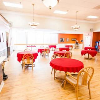 A brightly lit dining room with tables covered in red tablecloths and wooden chairs.