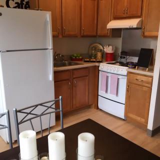 A cozy kitchen with wooden cabinets, featuring a refrigerator and stove, next to a dining table adorned with candles.