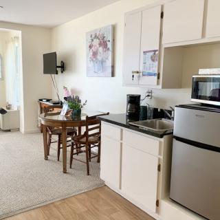 A modern apartment interior featuring a compact kitchen and dining area with a table, chairs, microwave, and fridge.