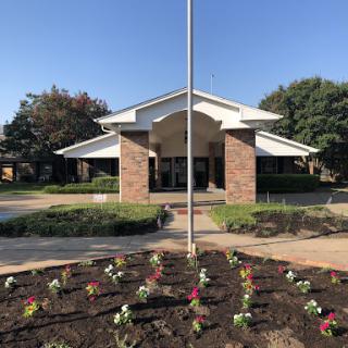 A well-maintained building with a landscaped entrance featuring colorful flowers and a flagpole.